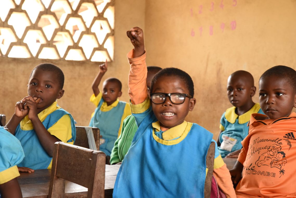 Die kleine Merveille aus Kamerun in der Schule, sie trägt eine Brille und zeigt gerade auf