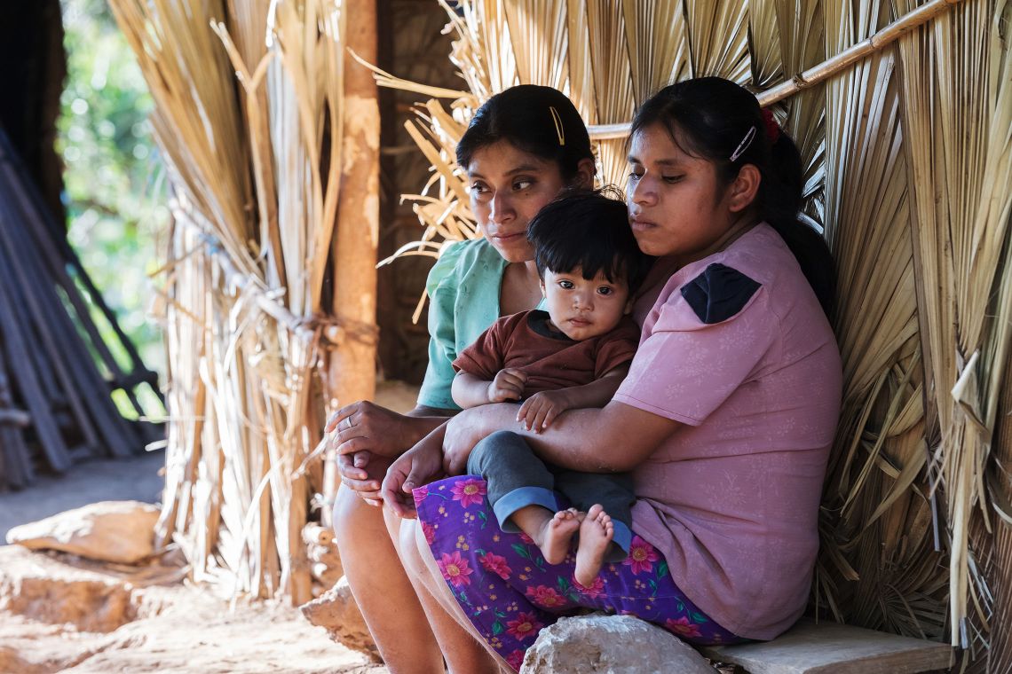 Zwei blinde Schwestern aus Guatemala sitzen vor ihrer Hütte. Eine der beiden hat einen kleinen Jungen auf dem Schoss.