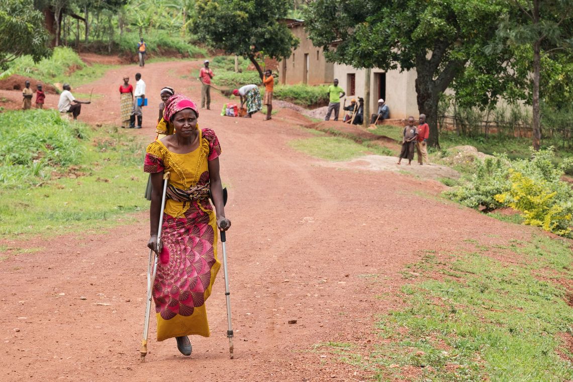 Einbeinige Frau aus Ruanda läuft auf Krücken durch ein Dorf