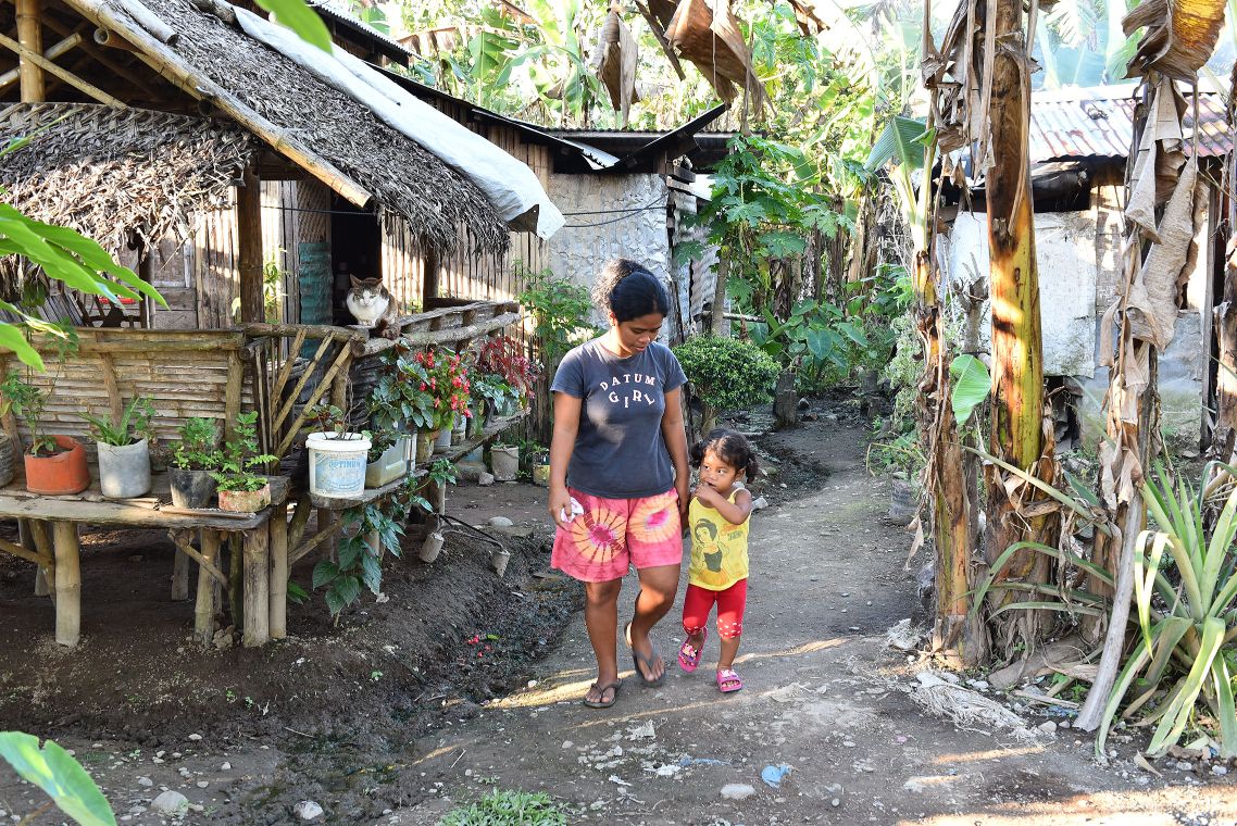 Philippinische Mutter läuft mit ihrer keinen Tochter einen Weg zwischen Hütten entlang.