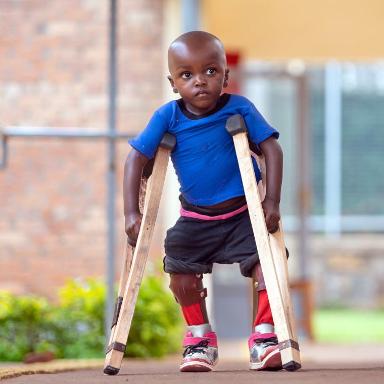 Ein kleiner Junge mit Beinschienen geht an Unterarmstützen aus Holz.