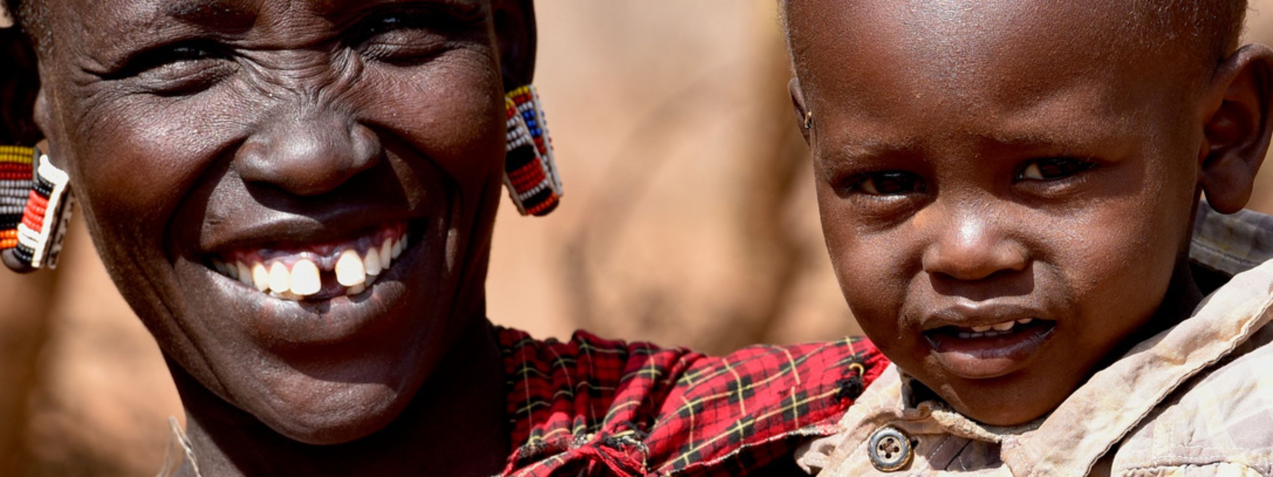 Eine lächelnde afrikanische Frau hat ein Kleinkind auf dem Arm.